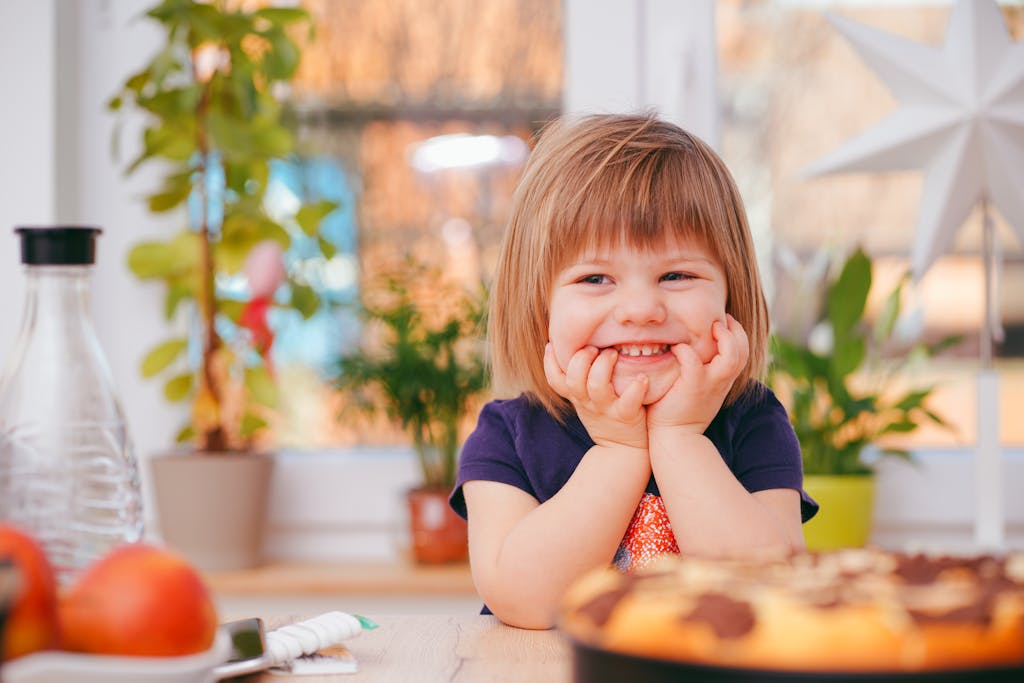 Smiling girl indoors with plants and pastry in natural sunlight.