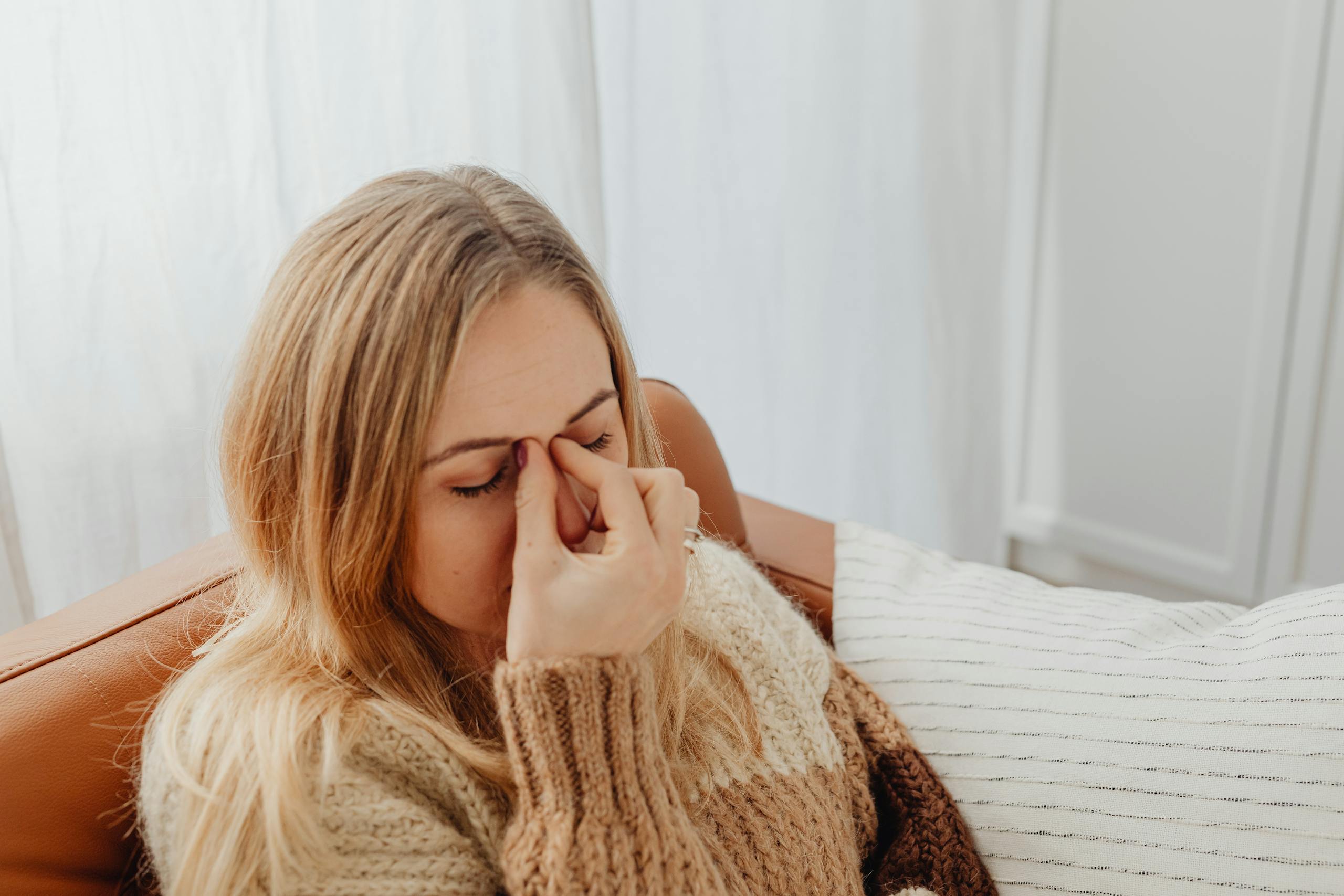AERD (Aspirin Exacerbated Respiratory Disease) A woman sitting on a couch with eyes closed, holding her nose in apparent sinus pain.