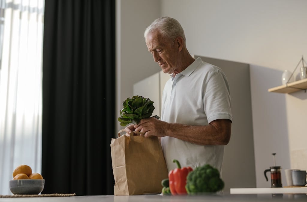 Elderly man unpacking fresh vegetables in a modern kitchen.